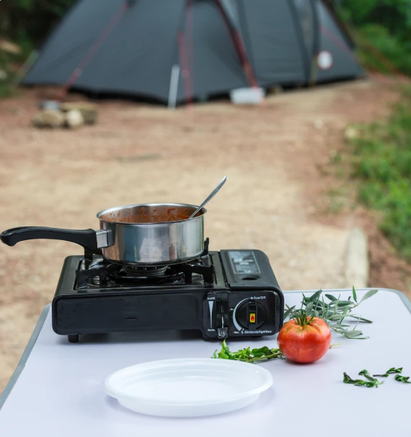 pot cooking on 1 burner camp stove on a white table and tent in background