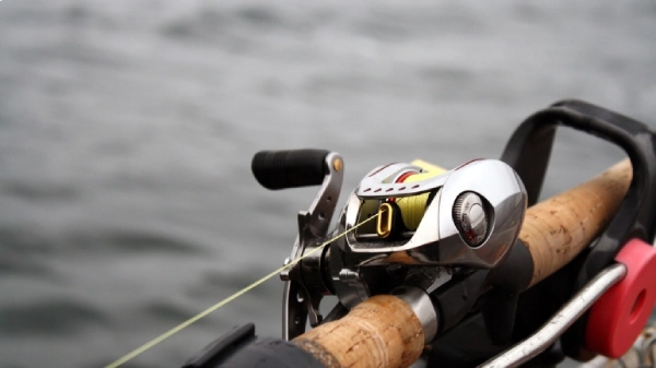 Closeup photo of a baitcasting reel attached to a fishing rod with water in background