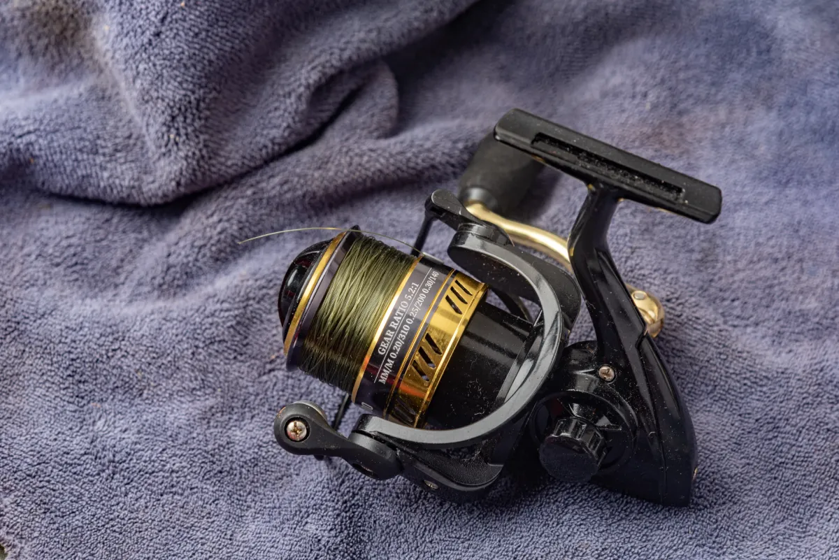 closeup of a black and gold colored fishing reel and a light purple cloth background