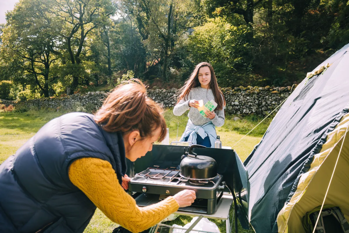 mother leaning down to light a cam stove and daughter walking toward her