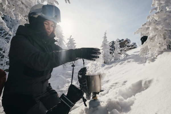 woman putting snow into solo camp stove to boil on mountain slope