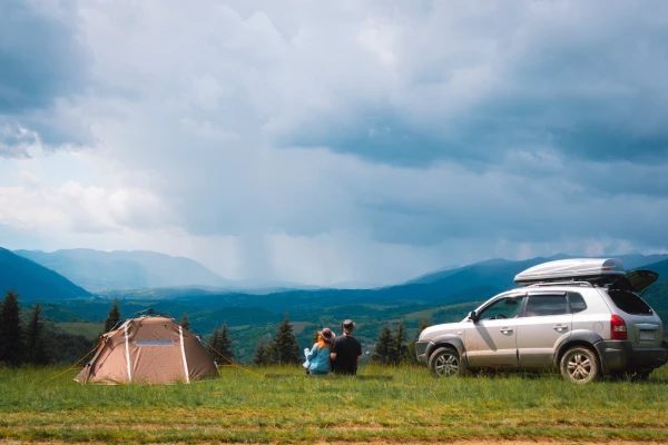 man and woman sitting between tent on left and a silver colored sport utility vehicle to the right