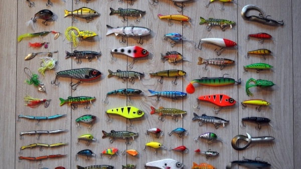 Many types of colorful fishing lures laying on a gray colored wood floor