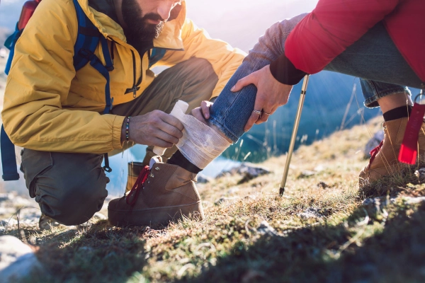 bearded male hiker wrapping bandage on ankle of female hiker on mountainside