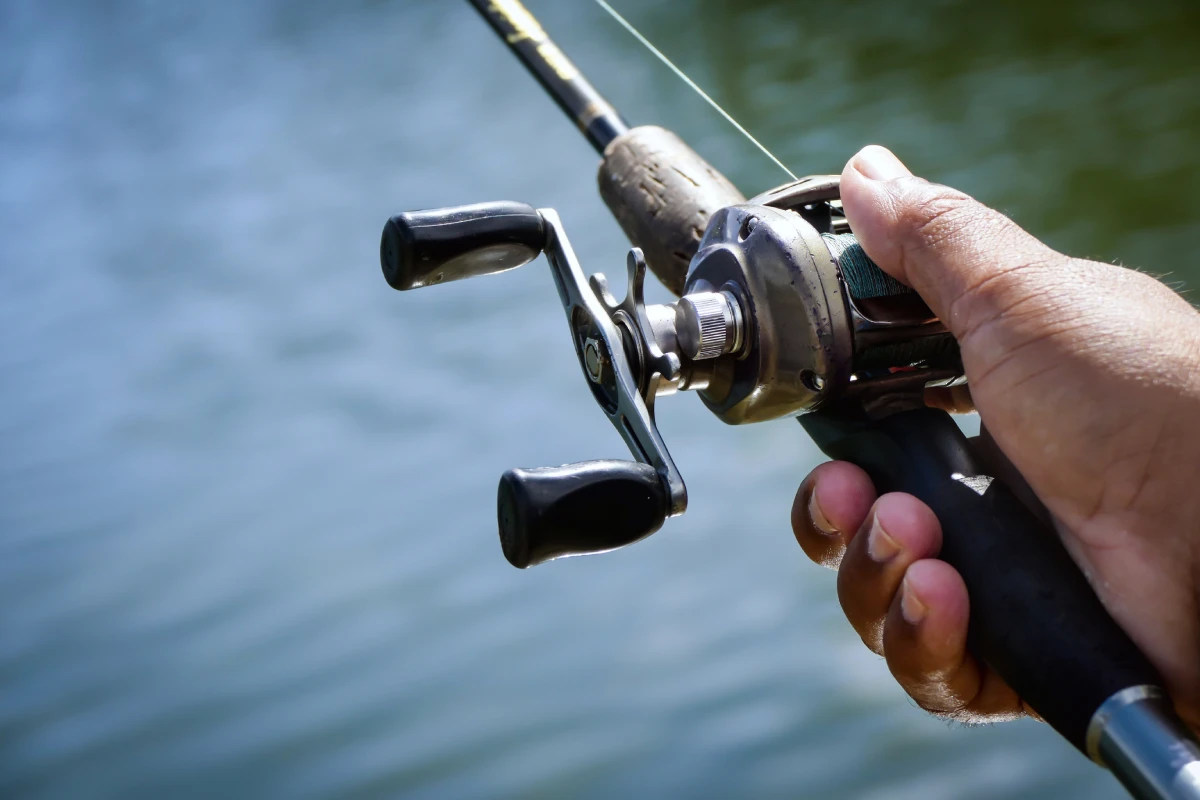 closeup photo of person holding a baitcasting reel on rod with water in background