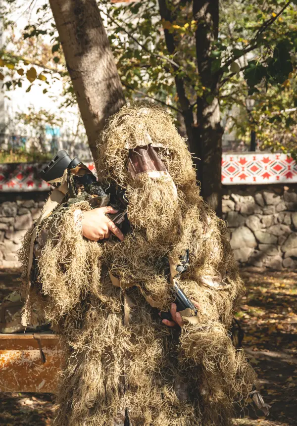 isolated photo of person holding gun wearing a tan colored ghillie suit