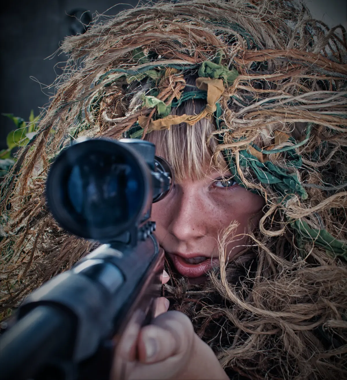 a woman in ghillie suit aiming a scoped rifle