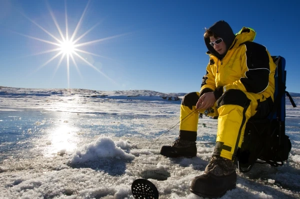 person wearing black and yellow snow suit ice fishing during a sunny day