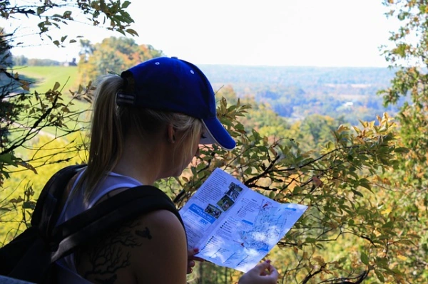 blue cap wearing blonde woman hiker looking a topographic map in forest