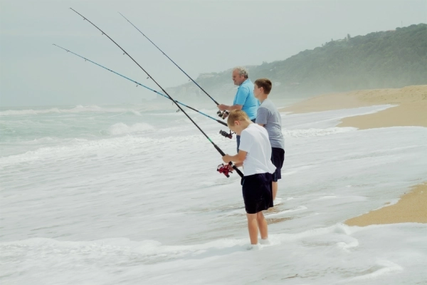 photo of a grandpa and grandsons fishing in ankle deep waves on a beach