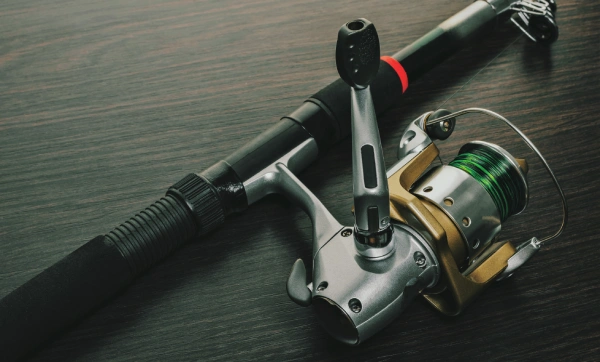 photo of a black fishing rod with gold and silver spinning reel with wooden background