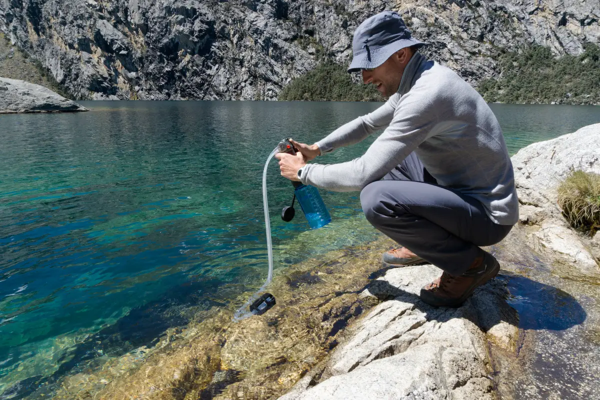 man using a outdoors water filter in a turquoise colored lake