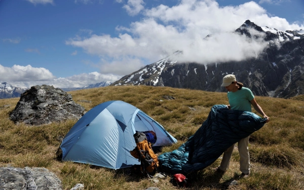 women packing up sleeping bag at alpine campsite