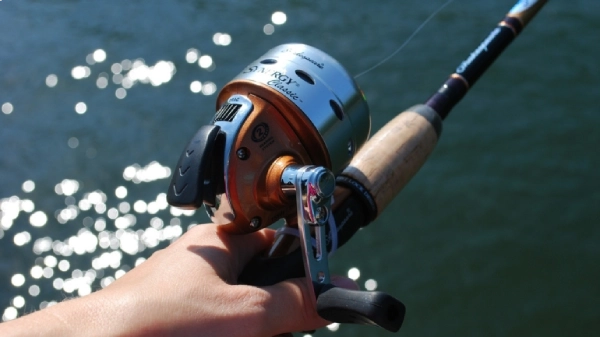 Closeup photo of a spin cast fishing reel being held by a hand over water