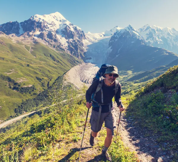 male hiker wearing a hat for sun protection on a trail with snowcapped mountains in background