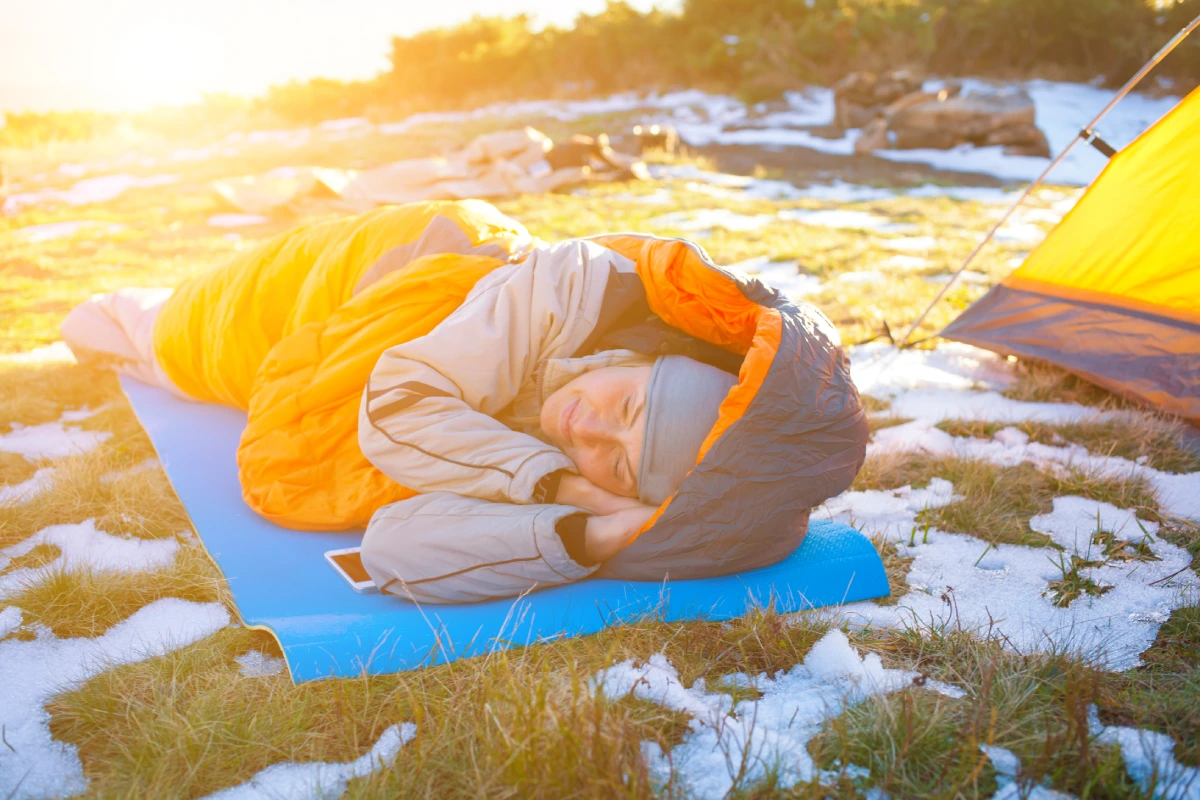 a blonde woman side sleeping in an orange sleeping bag