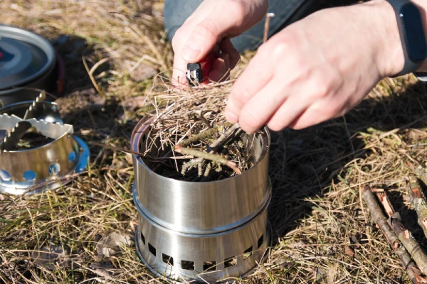 person igniting twig inside a metal wood burning camp stove