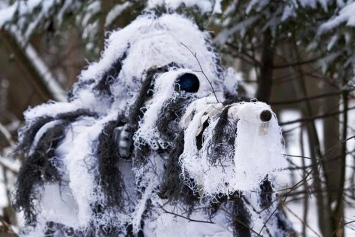 selective image of a person pointing a rifle while wearing a white and brown coloer ghillie suit