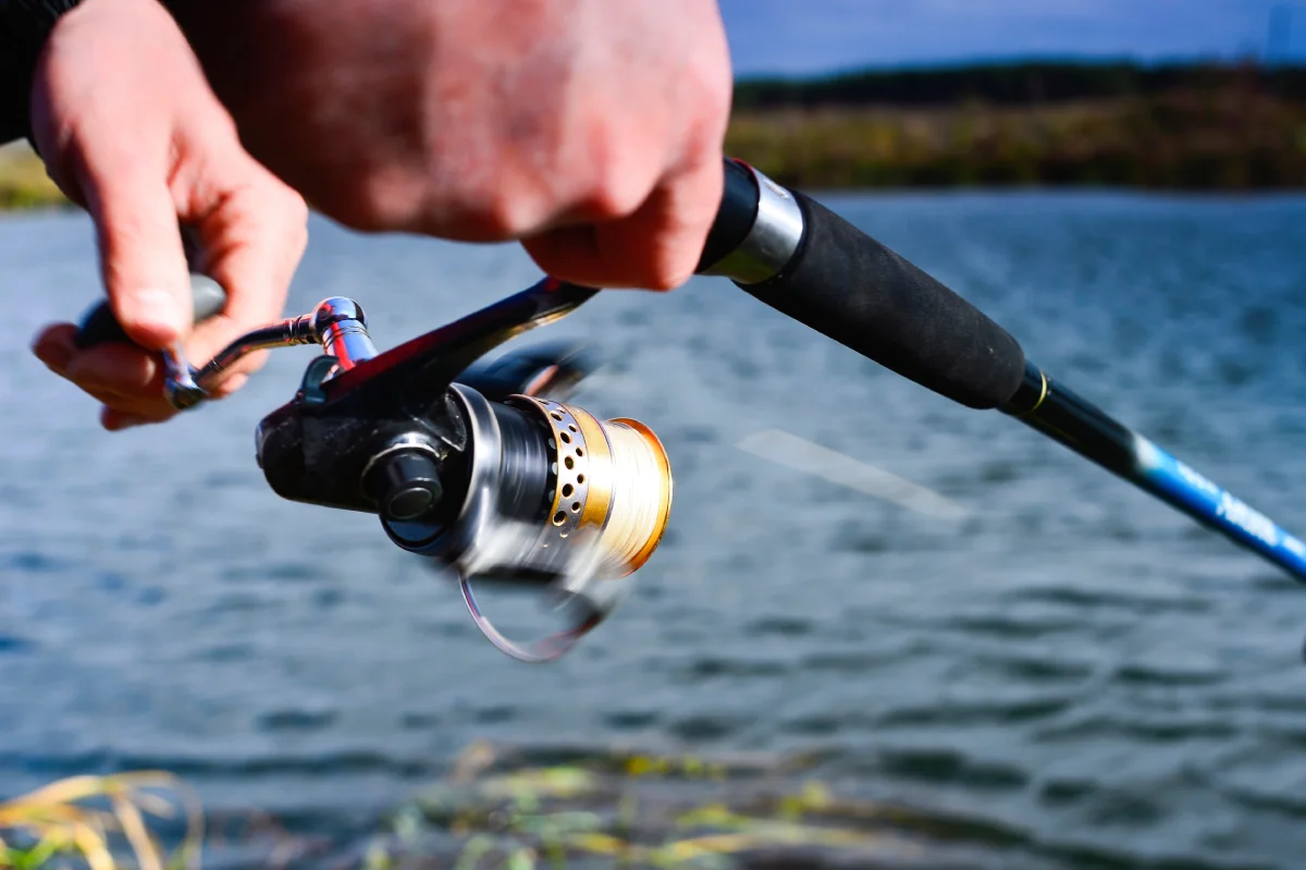 closeup photo person reeling a spinning reel with a lake in background