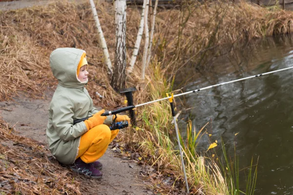 a child in warm clothing fishing by an autumn lake