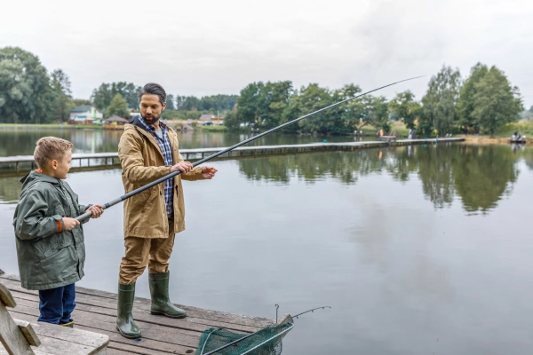 father show his son how to how fishing rod wear rain gear on a dock during autumn day