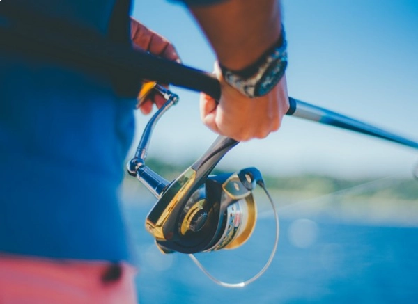 closeup photo of a person holding a rod and spinning reel with blurred bright background