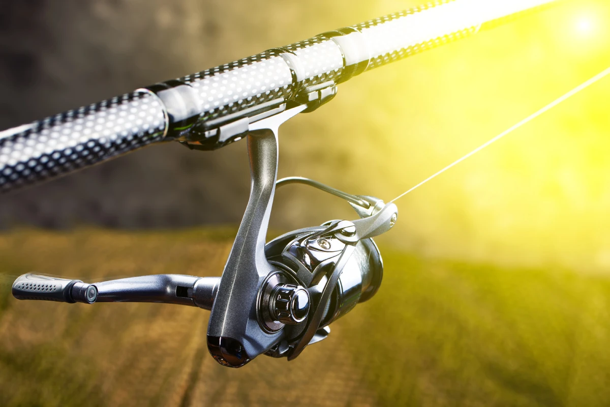 image of a side angle view of a silver spin reel on a rod with a burst of yellow light at the right top corner