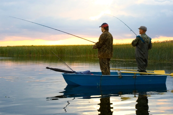 two fishermen in a blue boat on a sunrise lake